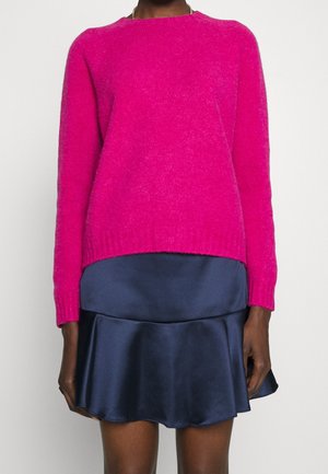 Personne portant un pull duveteux rose vif associé à une mini-jupe en satin bleu marine avec un ourlet à volants.