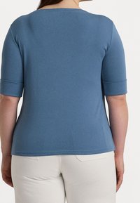 Blå kortärmad topp i ribbat tyg. Har en vid halsringning och uppvikta ärmar. Bärs med ljusa byxor som ger en avslappnad stil.