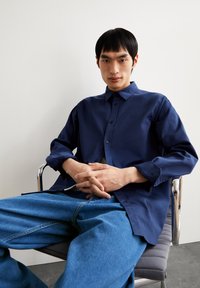 Donkerblauw overhemd met knopen van gladde stof, met lange mouwen en een klassieke kraag, gecombineerd met lichtblauwe spijkerbroek.