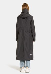 Lång svart regnkappa med huva, tillverkad av vattentåligt material, med elastisk midja och reflextape vid fållen.