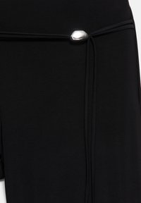 Tissu noir avec un fin cordon noir noué à travers une perle ovale argentée brillante sur un détail de vêtement.