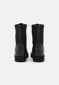 Botas de tobillo negras con una combinación de cuero liso y tejido elástico. Presentan una puntera redondeada y una suela de goma texturizada.