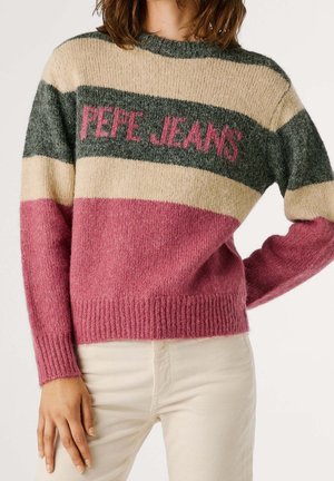 Kobieta ubrana w kolorowy, puszysty sweter z napisem "PEPE JEANS" w odcieniach różu, szarości, beżu i różowego, zestawiony z jasnymi spodniami.