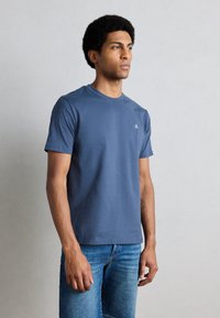 Niebieska bawełniana koszulka z okrągłym dekoltem, krótkimi rękawami i małym logo na lewej piersi, w połączeniu z niebieskimi jeansami.