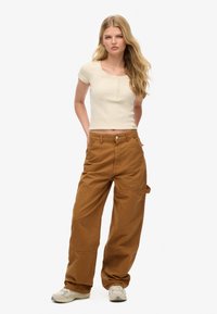 Top ajustado color beige claro con mangas cortas y detalle de botones, combinado con pantalones cargo sueltos marrones que tienen bolsillos laterales y una textura suave.