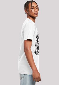 Hvit bomull t-skjorte med svart grafisk design på forsiden, kortermet, og en avslappet passform. Blå jeans brukes sammen med den.