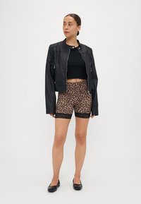 Svart cropped skinnjakke, svart ribbet topp og leopardmønstrede shorts med blondedetaljer. Modellen har på seg svarte leiligheter og står foran en ensfarget bakgrunn.