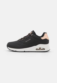 Scarpa sportiva nera con upper sintetico testurizzato, chiusura con lacci, un accento in rosè oro, intersuola bianca e dettaglio in air cushion trasparente.