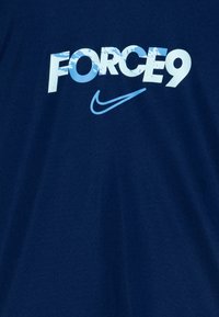 T-shirt bleu marine avec le texte audacieux en blanc et bleu clair "FORCE9" ainsi que le logo Swoosh de Nike. Tissu doux avec un col rond.
