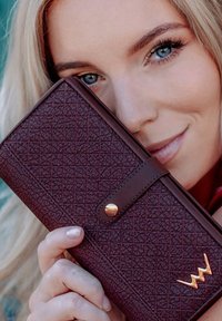 Maroon wallet with a textured pattern, featuring a brown strap and gold-colored snap button, along with a gold logo accent.