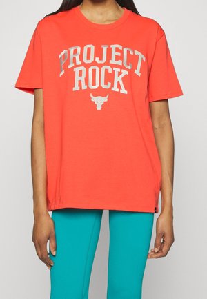 Vrouw draagt een losse feloranje T-shirt met "PROJECT ROCK" en een stierenlogo, gecombineerd met strakke turquoise legging.