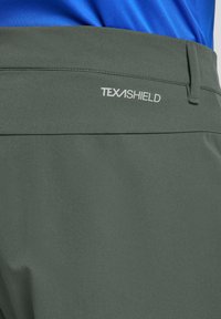 Pantalon TEXASHIELD vert avec une texture lisse, doté d'une poche arrière et d'un logo blanc sur la ceinture.