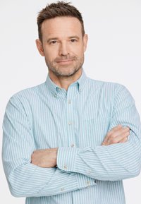Camicia button-down azzurro chiaro con strisce bianche, maniche lunghe e taschino sul petto. Presenta bottoni dorati e una texture in cotone liscia.