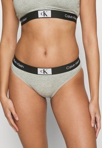 Szürke pamut alsónadrág fekete derékkal, amelyen fehér "Calvin Klein" márkázás és logó található. Puha tapintású, alacsony derekú kialakítás.