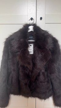 Braune Kunstpelzjacke mit lockerem Kragen, langen Ärmeln und einer weichen, strukturierten Oberfläche. Das Etikett zeigt Größe M und die Markenbezeichnung Bershka.