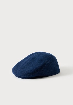 Casquette plate en laine bleu marine avec coutures apparentes, présentée sur une surface claire unie, vue de côté.