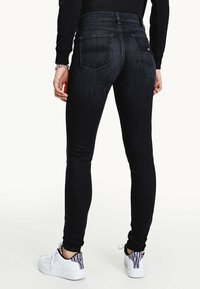 Svarta smala jeans med hög midja, två bakfickor och en mjuk denimtextur. Bärs med vita sneakers med ett mönstrat klack.