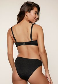Schwarzes Bikini-Set aus einem strukturierten Stoff mit einem dezenten Muster, verstellbaren Trägern und einem Verschluss auf der Rückseite. Hoch geschnittener Bikiniunterteil.