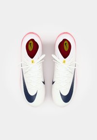 White athletic shoes with navy blue accents, round pink rubber soles, and white laces. Includes Nike logo on the side and insoles.