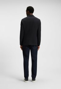 Marinblazer i ett strukturerat tyg, modern passform, en bakre slits och krollappade slag, som matchas med mörka jeans och vita sneakers.