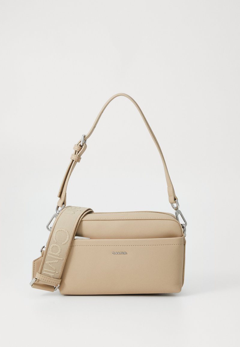 Beżowa torba na ramię wykonana z gładkiego materiału, z odczepianym wzorzystym paskiem, srebrnymi akcentami i eleganckim prostokątnym kształtem.