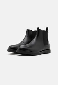 Botas Chelsea de cuero negro con textura suave, paneles laterales elásticos, puntera redonda y lengüetas en la parte trasera para facilitar el calzado. Suela plana de goma.