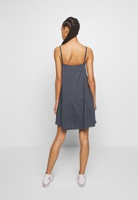 Námořnická modrá bezramenná šaty s volným střihem, vyrobené z měkké tkaniny. Obsahuje tenké nastavitelné ramínka a zaoblený design zad.
