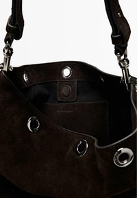 Interno di una borsa tote in camoscio marrone scuro con ferramenta argentata, dotata di occhielli metallici e chiusura a scatto. Include una fodera in tessuto nero.