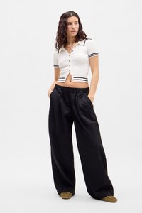 Cardigan scurt cu mâneci scurte, din tricot alb cu dungi negre și nasturi aurii; asortat cu o pereche de pantaloni negri largi.