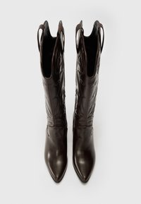 Bottes de cow-boy en cuir marron avec des pointes acérées et des coutures décoratives. Caractéristiques des tiges hautes avec des découpes pour le style et le confort d'utilisation.