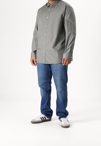Camisa de manga larga con cuello en gris claro, diseño de botones, combinada con vaqueros de mezclilla azules y zapatillas blancas con rayas negras.