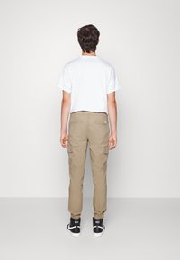 Lätt vit bomullströja i kombination med khaki cargo-byxor med sidofickor och elastiska avslut, kompletterat med svarta högskurna sneakers.