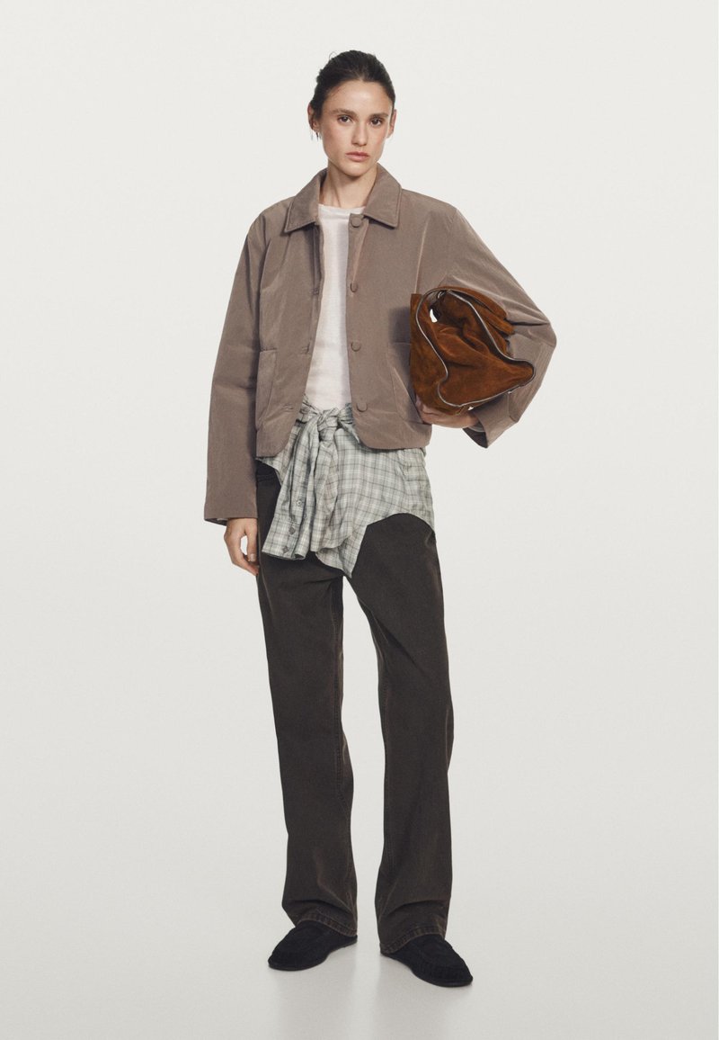 Brown corduroy jacket, white long-sleeve shirt, gray plaid tied around waist, dark pants, holding brown suede bag, black slippers.
