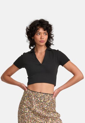 Zwarte cropped polo shirt met korte mouwen, met een V-hals en ribbelstructuur. Gecombineerd met een rok met bloemmotief, afgewerkt met een zwarte rand.