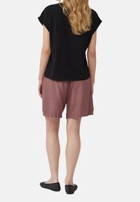 Zwart T-shirt met korte mouwen, lichtroze shorts en zwarte instapschoenen. De stoffen lijken zacht; het shirt heeft omgeslagen mouwen en de shorts hebben een elastische tailleband.