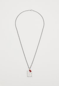 Ασημένια αλυσίδα λαιμού με ορθογώνιο φυλαχτό με ανάγλυφα σχέδια και μια μικρή κόκκινη ετικέτα. Η αλυσίδα έχει υφή.