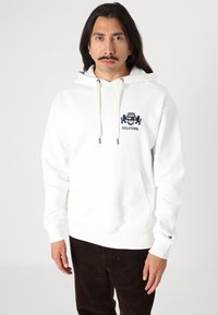 Weißer Kapuzenpullover aus Baumwollmischung, mit einer Fronttasche und einem gestickten Logo in Marineblau. Die Ärmel haben gerippte Bündchen mit Logo-Akzent.