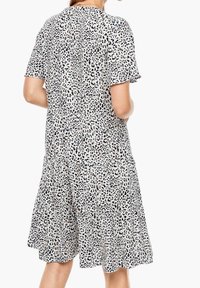 Kortärmad, A-linjeformad klänning i krämfärg med svart leopardmönster. Har en lager-på-lager kjol och rund halsringning. Mjuk, lätt tyg.