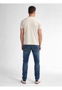Camiseta de manga corta color beige claro, con forma ajustada, combinada con jeans de mezclilla azules que tienen bolsillos y piernas ajustadas, complementada con zapatos blancos.