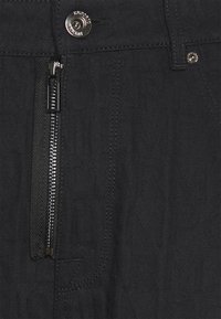 Czarna dżinsowa tkanina z wytłoczonymi literami, metalowy zamek błyskawiczny oraz błyszczący guzik zapięcia na spodniach.