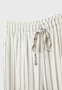 Pantalon léger de couleur crème avec des rayures noires verticales, doté d'une ceinture élastique et d'un cordon de serrage.