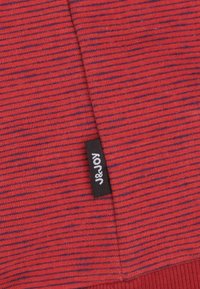 Rood en blauw gestreepte stof met een zachte textuur, met een zwart label met witte tekst "J&JOY" aan de rand.