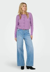 Lila knapp-up cardigan med långa ärmar, i kombination med ljusblå vida jeans och svarta klackade ankelstövlar. Släta texturer genom hela outfiten.