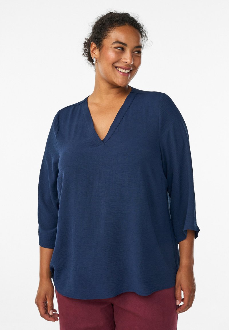 Haut bleu marine à col en V avec des manches 3/4, confectionné en tissu texturé. Forme fluide avec une coupe décontractée, sans motifs ni embellissements visibles.