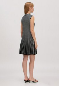 Schwarz-weiß gestreiftes ärmelloses Kleid mit tailliertem Oberteil und schwingendem Rock, aus glattem Stoff gefertigt. Minimalistisches Design.
