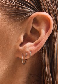 Silberne Creolen in drei Größen werden am unteren Ohrläppchen getragen und zeigen ein glänzendes metallisches Finish mit dezenten Reflexionen.