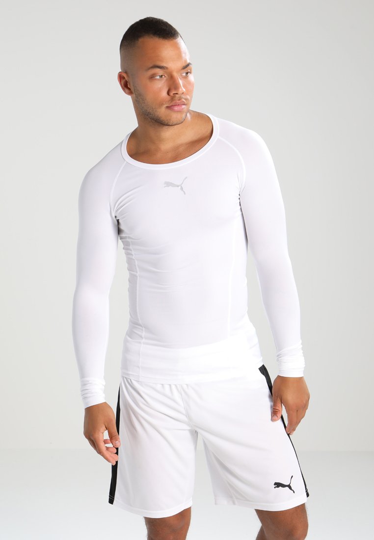Chemise de sport à manches longues blanche avec un col rond, design ajusté, et logo Puma sur la poitrine. Portée avec un short blanc assorti.