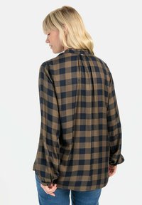 Bruine en marineblauwe geblokte blouse met lange mouwen, ruches bij de halslijn en een plissé-detail op de rug. Zachte stof en getailleerde manchetten met knopen.