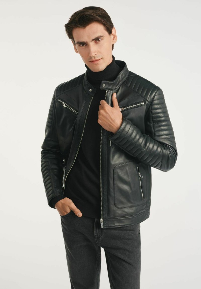 Czarna skórzana kurtka z pikowaną wyściółką na ramionach, zamykanymi kieszeniami i stójką. Noszona na golf, w połączeniu z szarymi dżinsami.