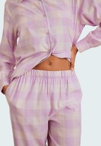 Ljuslila rutig pyjamasset med en knäppskjorta och byxor med elastisk midja, med vita och ljuslavendelfärgade rutor.